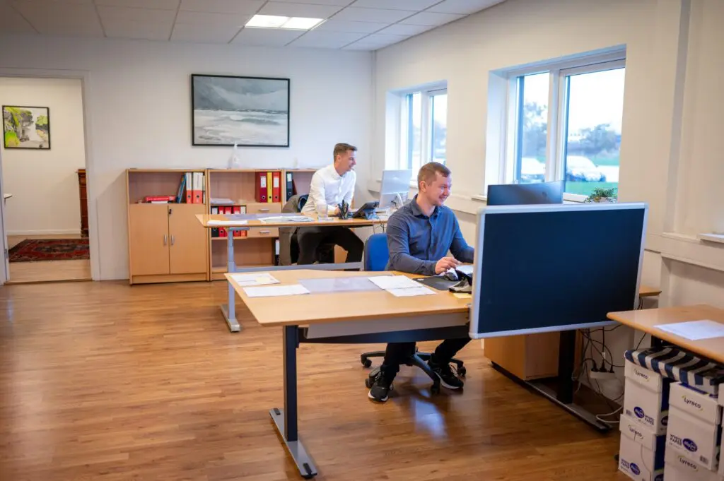 To mænd arbejder ved computere på et kontor hos Behrens Logistik, der tilbyder lager- og distributionsløsninger.