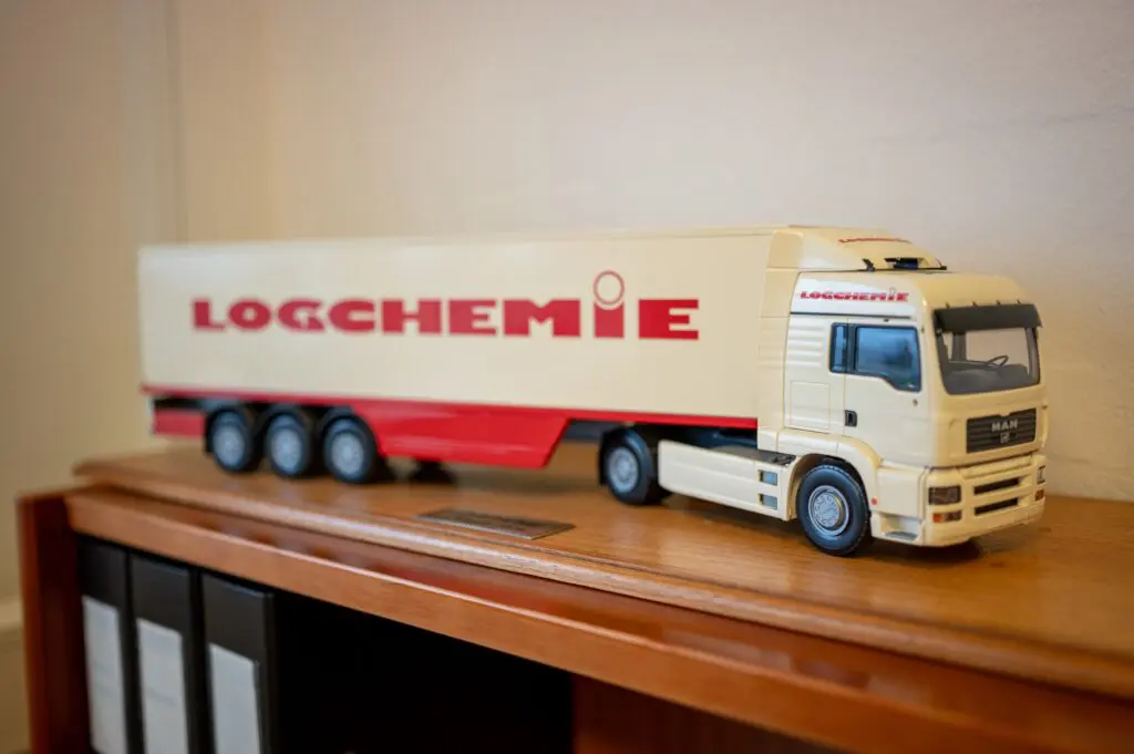 Model af en hvid og rød lastbil med "LOGCHEMIE" på siden, der repræsenterer Behrens Logistiks transportløsninger.
