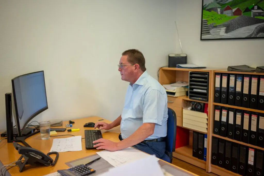 Mand arbejder ved computer på kontor hos Behrens Logistik, omgivet af arkivskabe og logistikudstyr.