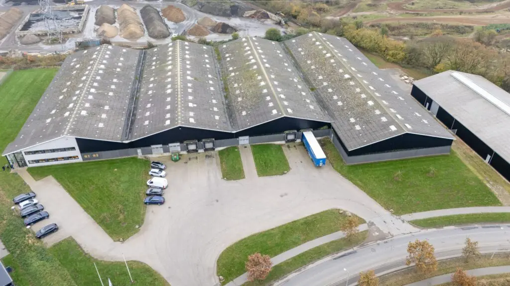Luftfoto af Behrens Logistik's store lagerbygninger med lastbiler og varevogne parkeret.