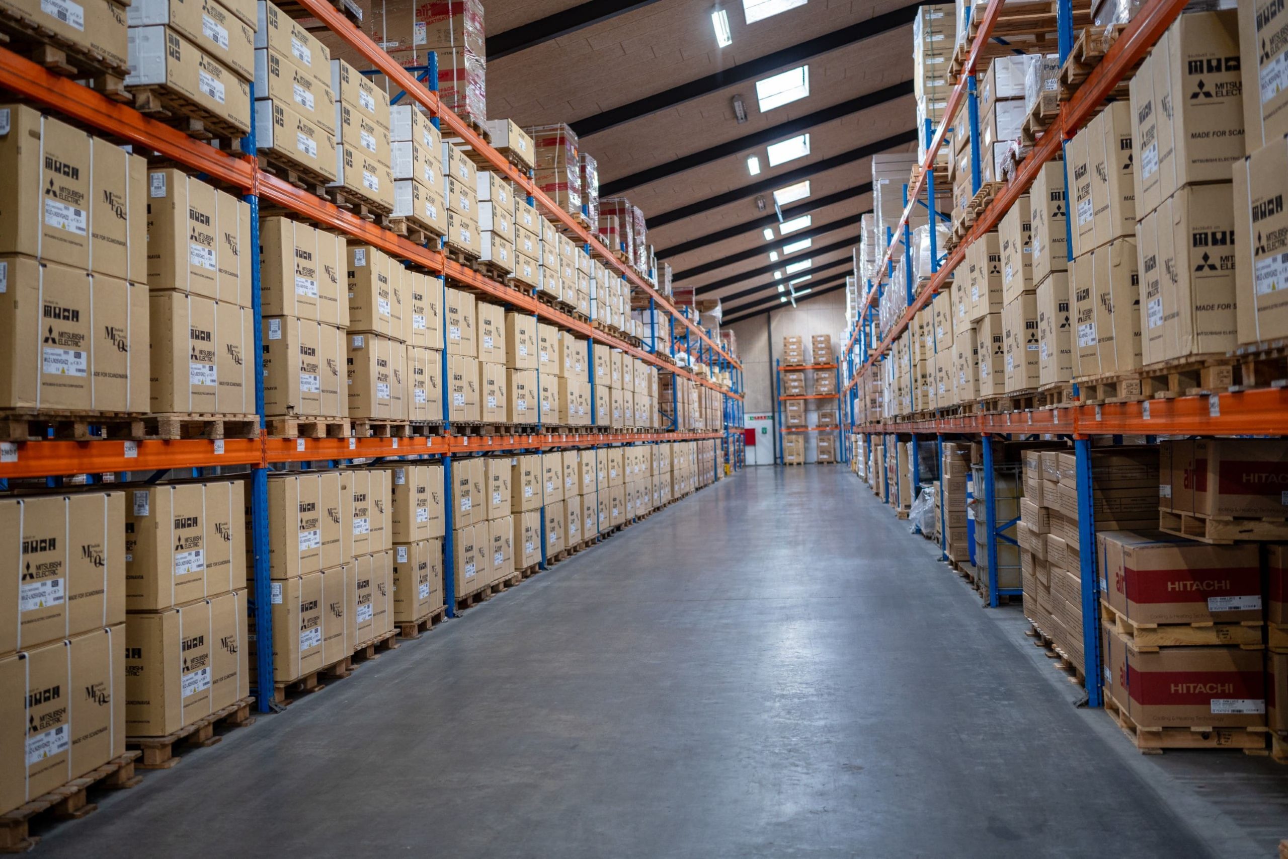 Moderne lagerhal hos Behrens Logistik med høje reoler fyldt med paller og kasser, klar til distribution.