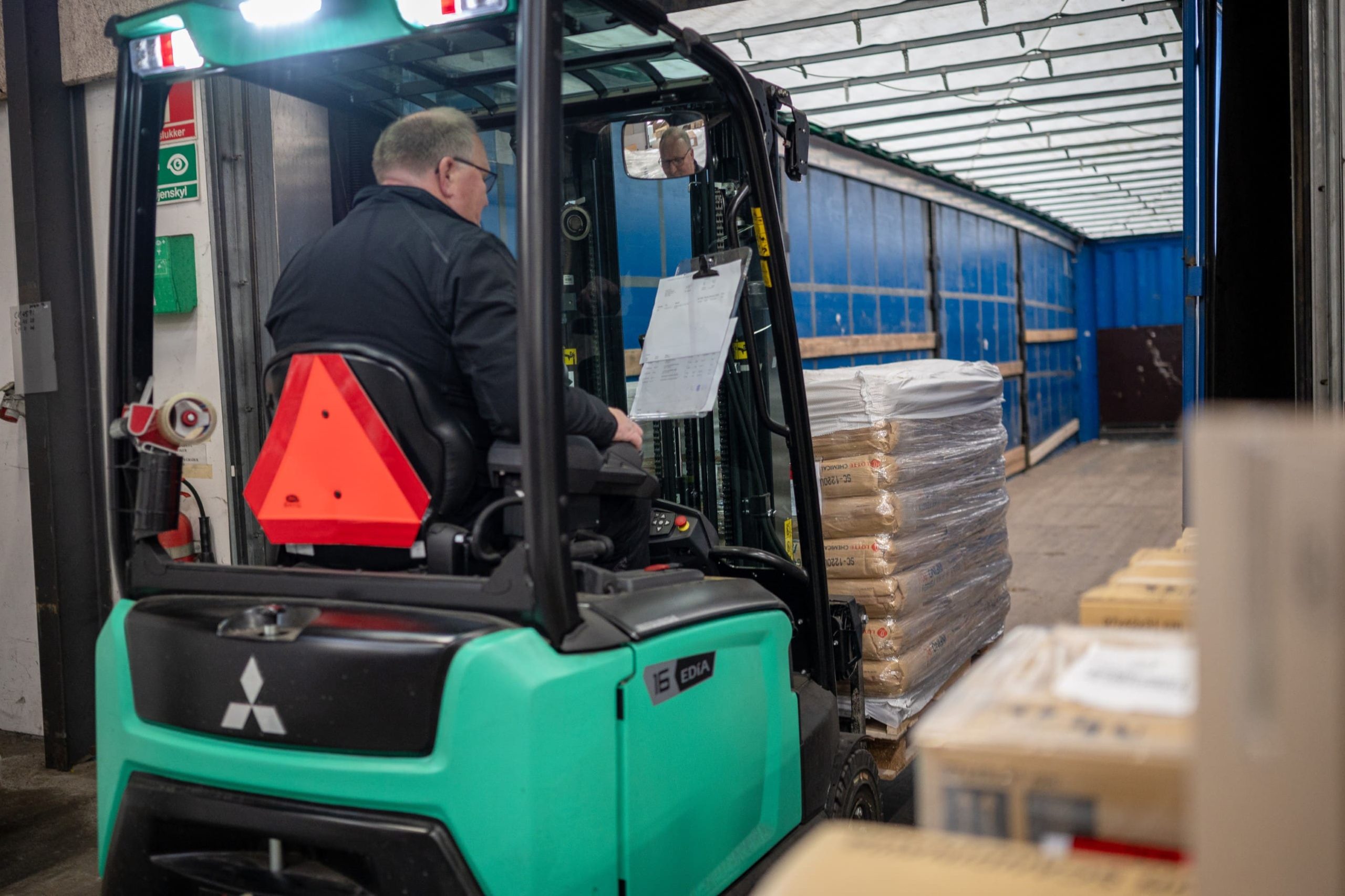 Medarbejder i Behrens Logistik betjener en grøn gaffeltruck, der transporterer pallevare i et lager.